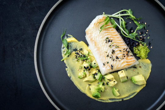 Gourmet Kabeljau Fisch Filet gebraten mit Kaviar, Avocado Scheiben und Mango Senf Creme als Draufsicht auf einem Modern Design Teller mit Textfreiraum links