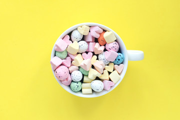 Sweet marshmallows and candies in a cup on a bright yellow background, top view. Easter concept