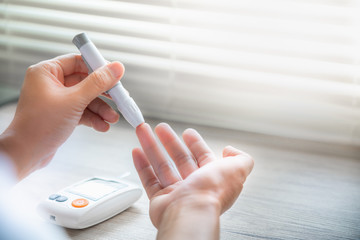 Closeup woman hands using lancet on finger to check blood sugar level by Glucose meter, Healthcare Medical Check up, Medicine, diabetes, hyperglycemia concept - obrazy, fototapety, plakaty