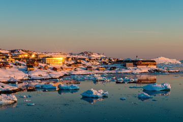 Glacier-filled waters and a snowy artic village at sunset, Greenland.