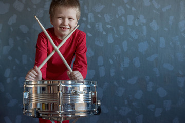 Teen boy in red suit playing drum in room. child holds drumsticks