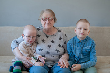 elderly woman sits and plays with her grandchildren on couch. Children love grandmother very much....