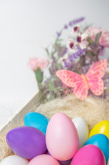 Obraz na płótnie Canvas Colored Easter eggs and flowers in wooden white box with pink butterfly on white background .