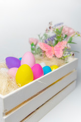 Colored Easter eggs and flowers in wooden white box with pink butterfly  on white background .