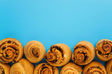 Multiple rolled bun with cinnamon, nuts and raisins on blue background with copy space