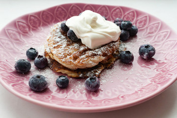 Low Carb Keto Diet Pancakes from almond coconut flour with blueberries, sour cream on pink plate background close up view. Selective focus. Copy space. Ketogenic concept