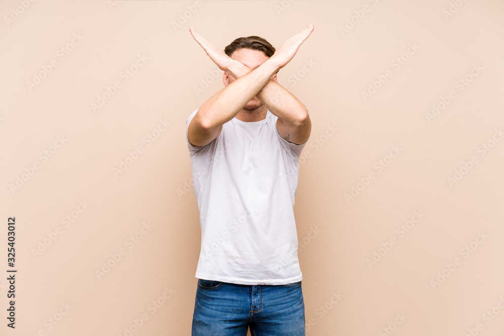 Wall mural young caucasian man posing isolated keeping two arms crossed, denial concept.