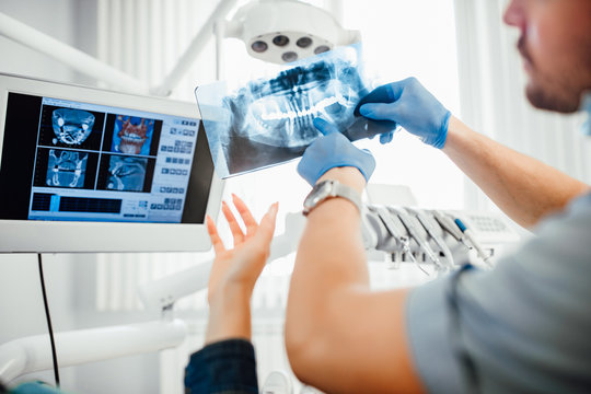 Medicine, dentistry and healthcare concept, dentist showing teeth x-ray to female patient at dental clinic office.