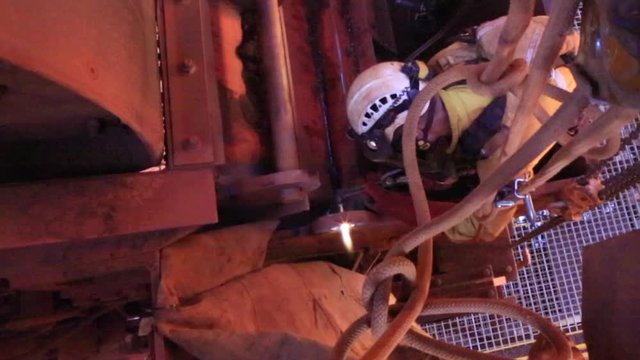 Top view footage of rope access welder wearing safety equipment, glove protection working on twin rope working fall arrest position conduct oxy cutting lifting lug metal repairs on construction site