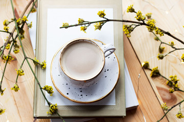 Cup of coffee and a book on a wooden background with yellow flowers. Workplace. Cozy breakfast. Spring concept