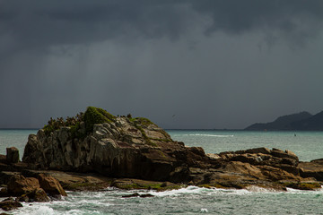 Dramatic shot of sea rocks and rain clouds over the ocean in the background. Armação Beach