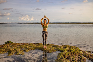 Yoga pose. Woman practicing yoga at the beach. Young woman standing and raising arms with namaste...