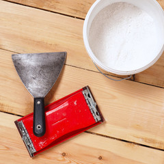 A trowel and an emery grater are on the floor. Nearby is a bucket of plaster gypsum. The floor of...