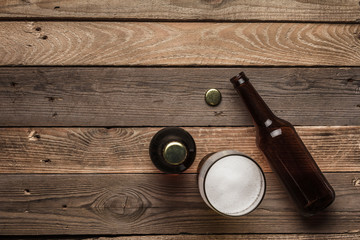 Two dark beer bottles and a glass of beer and foam on a wooden background.