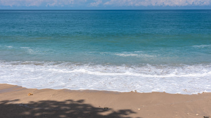 Sand beach with wave bubbles, blue sea and sky