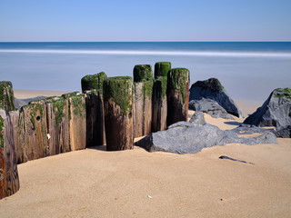 Old wood pilings worn and damaged by years of storms sit on a deserted winter beach in the New...