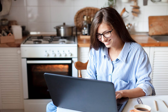 Young woman working from home office. Freelancer using laptop and the Internet for shopping online. Happy girl smiling. Workplace in cozy kitchen. Successful female business. Lifestyle moment.