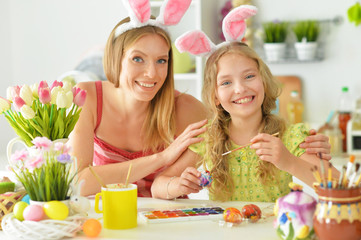 Mother with daughter wearing rabbit ears decorating Easter eggs