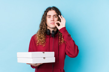 Young caucasian man holding pizzas isolated with fingers on lips keeping a secret.
