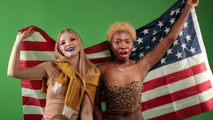 Happy young girls african american and european with american flag with good mood standing and raising hands