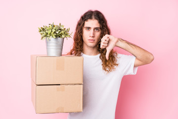 Young caucasian man holding boxes isolated showing a dislike gesture, thumbs down. Disagreement...