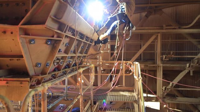 Footage of rope access welder abseiler wearing full safety harness, helmet, mask protection uniform abseiling working on twin ropes commencing hot work gouging  construction mine site, Perth Australia