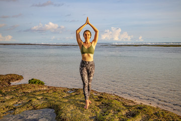 Yoga pose. Woman practicing yoga at the beach. Young woman standing and raising arms with namaste...