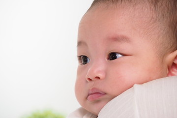 Closeup of a child face looking at something curiously after waking up in the morning cradled by his mother with love. Cute innocent Asian baby with facial expression and healthy childhood concept