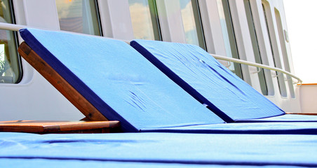 Wooden teak deck chairs and sun loungers with blue  pillows and upholstery on deck of luxury...