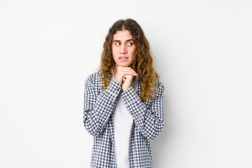 Young long hair man posing isolated keeps hands under chin, is looking happily aside.