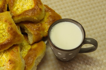  On a beige tablecloth there is a gray ceramic cup with milk and homemade cakes: fresh curd cheesecakes.
