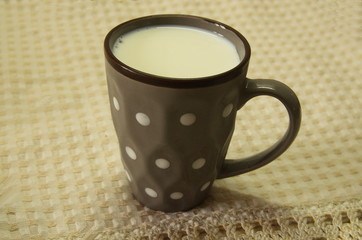  A napkin lies on the table and there is a gray ceramic cup with fresh, cool milk.