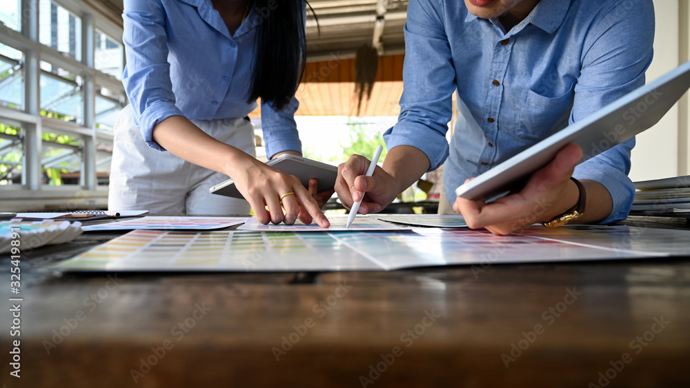 Poster cropped image of graphic designer discussing at the wooden meeting table with working stuff.