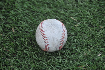 a old used white baseball sitting on a artificial turf field