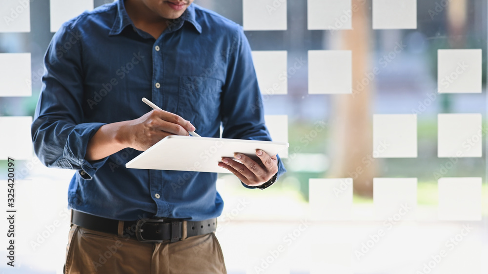 Poster a man using/holding computer tablet and stylus pen while standing in office.