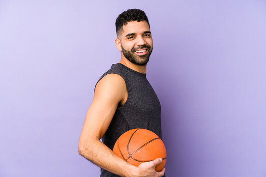 Young latin man playing basket isolated looks aside smiling, cheerful and pleasant.