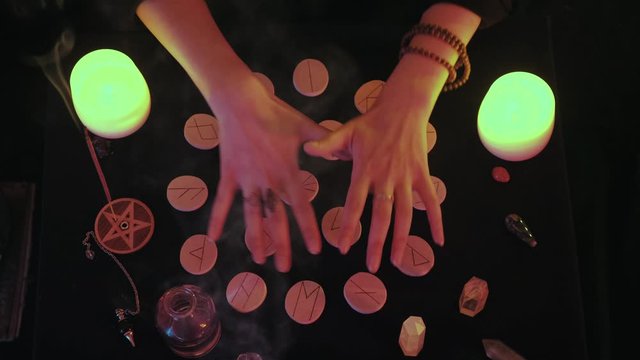 Medium top view shot of witchy hands fortune spelling over the runes 