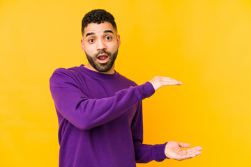 Young mixed race arabic man isolated shocked and amazed holding a copy space between hands.