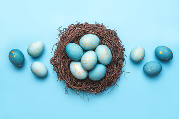 Easter eggs in nest on blue background. Flat lay, top view.