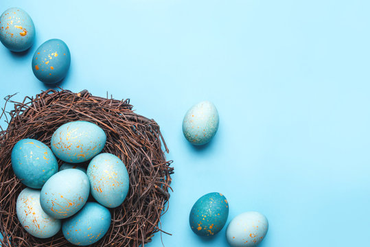 Easter eggs in nest on blue background. Flat lay, top view.