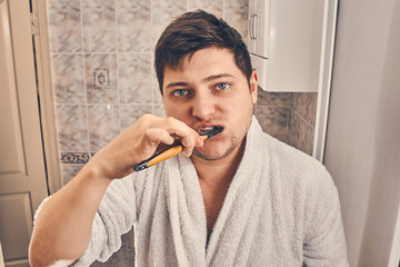 a man in a white coat is brushing his teeth in the bathroom.
