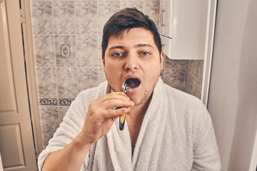 a man in a white coat is brushing his teeth in the bathroom.