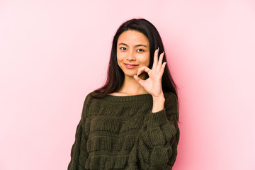 Young chinese woman isolated on a pink background cheerful and confident showing ok gesture.