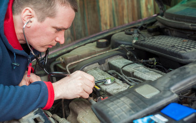 man with stethoscope checking car engine, auto service concept