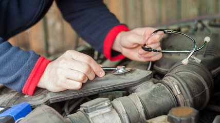 Fototapeta premium closeup of man's hand with stethoscope checking car engine, auto service concept