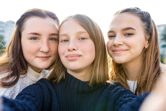 Close-up portrait, three girls schoolgirls teenagers, summer outdoors. Photography on phone, selfie photo, online app smartphone, networks on Internet. Emotions of happiness smile, relaxation fun.