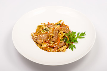 fetuccine pasta with fried chicken, red sweet pepper and sesame seeds in a white plate on a white background