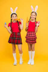 eating carrot. small girls bunny ears yellow background. funny little sister kids celebrate easter. egg hunt begin. traditional spring holiday. happy easter. spring is coming. happy childhood concept