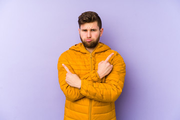 Young man isolated on purple background points sideways, is trying to choose between two options.