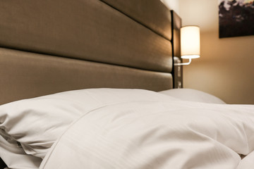 Fresh bedding seen on a luxury kings' sized bedroom in a premium-grade hotel. The modern lighting and soft headboard are evident.